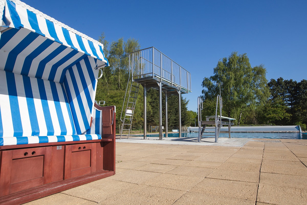 Im Vordergrund steht ein Strandkorb und im Hintergrund der 3 Meter und der 1 Meter Sprungturm.